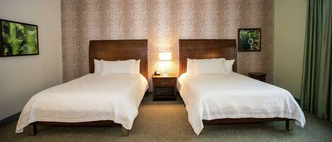 A hotel room with two beds, a nightstand with a lamp, and patterned wallpaper.