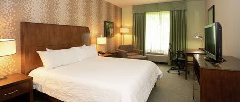 A hotel room with a large bed, a desk with a computer, a chair, a TV, and two lamps.