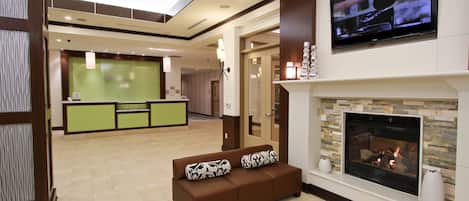 A hotel lobby with a reception desk, a fireplace, and a sofa with patterned cushions.