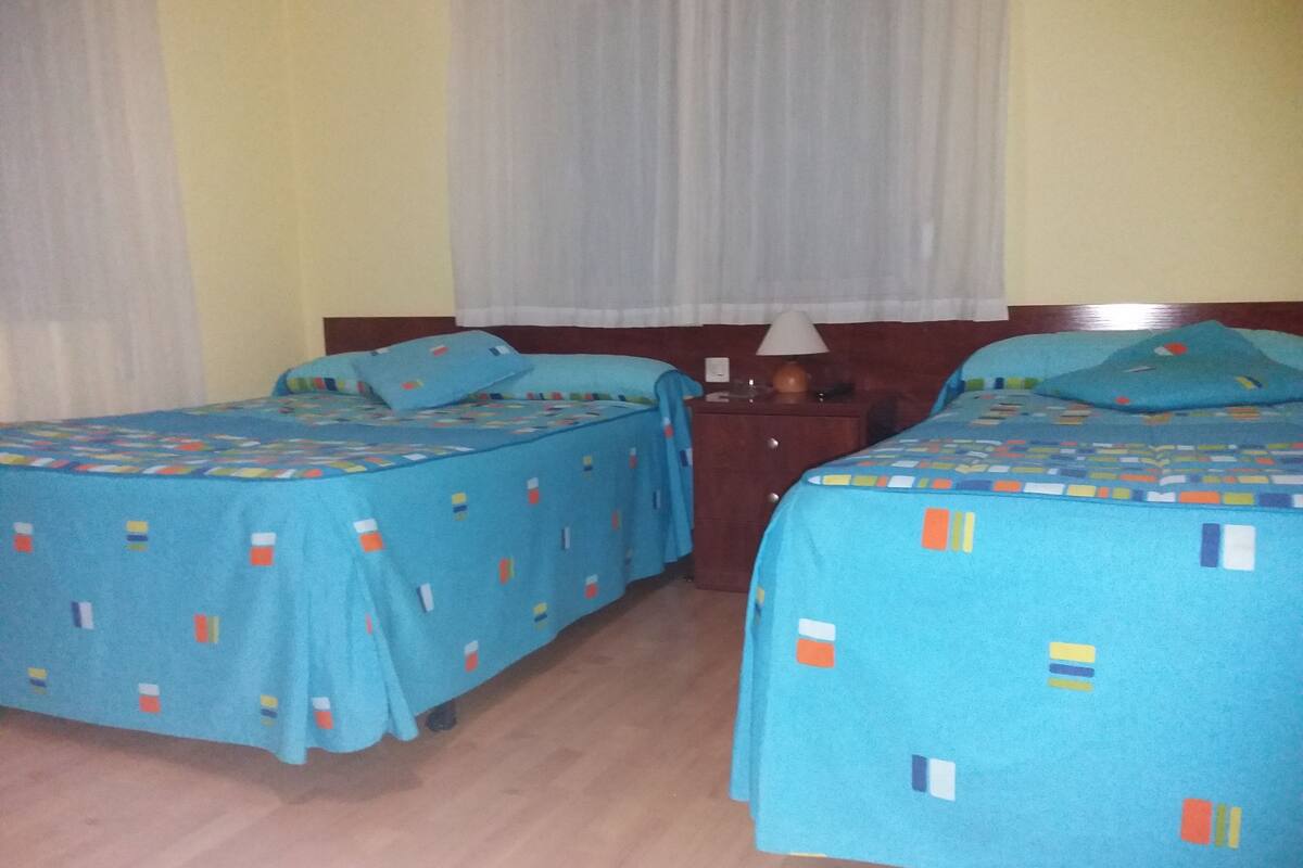 Two twin beds with blue bedding, a wooden nightstand, and a lamp between them.