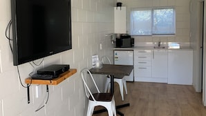 A compact kitchen with a dining area, a flat-screen TV mounted on the wall, and a small refrigerator.