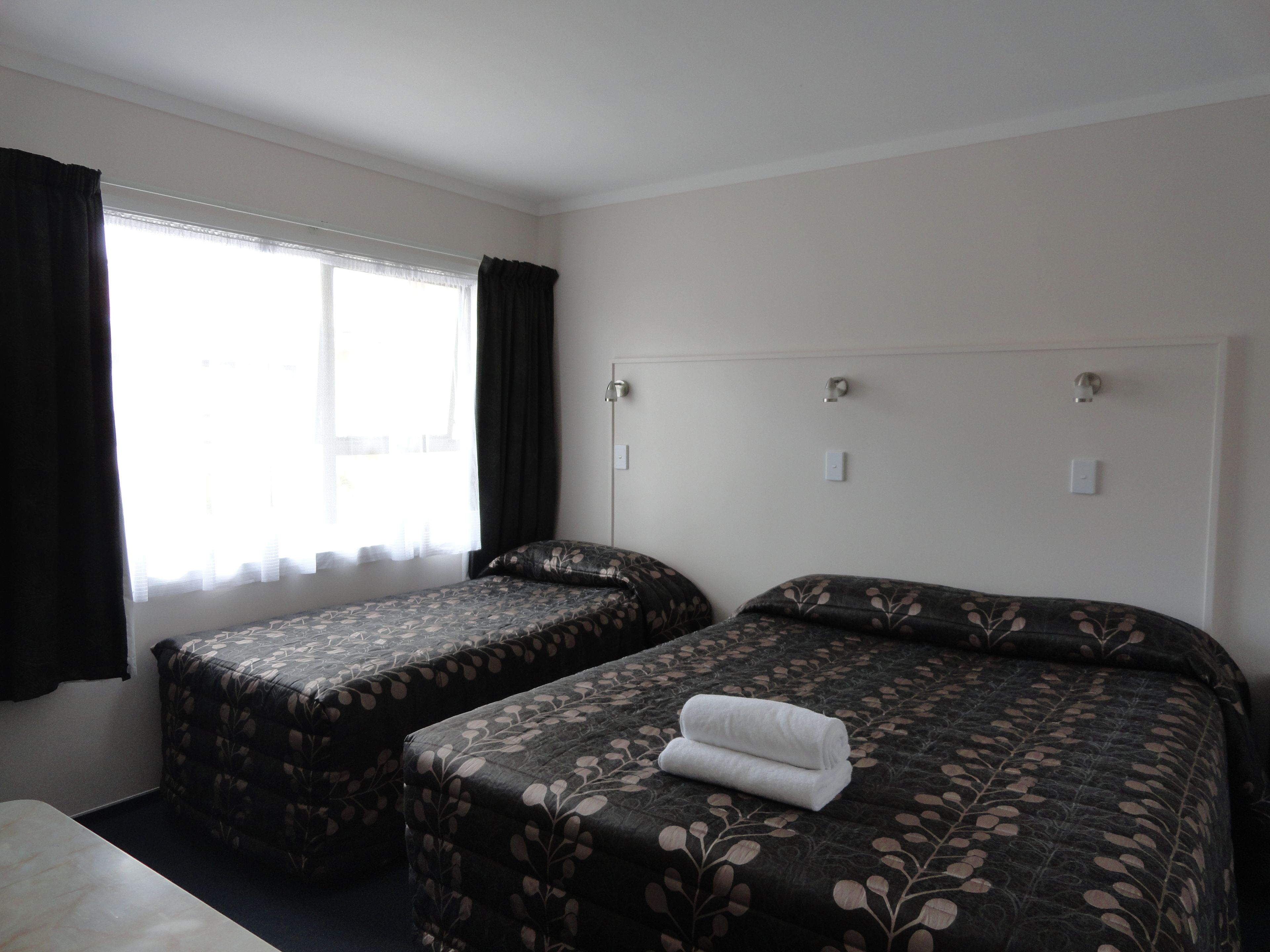 Een hotelkamer met twee bedden, een raam met gordijnen en een witte muur.