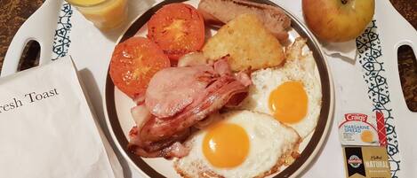Un plateau de petit-déjeuner avec des œufs, du bacon, des tomates, des toasts et une pomme.