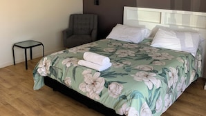 A bedroom with a bed, a chair, a small table, and a painting on the wall.