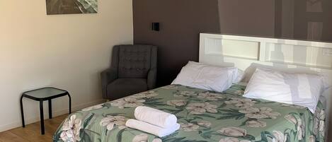 A bedroom with a bed, a chair, a small table, and a painting on the wall.