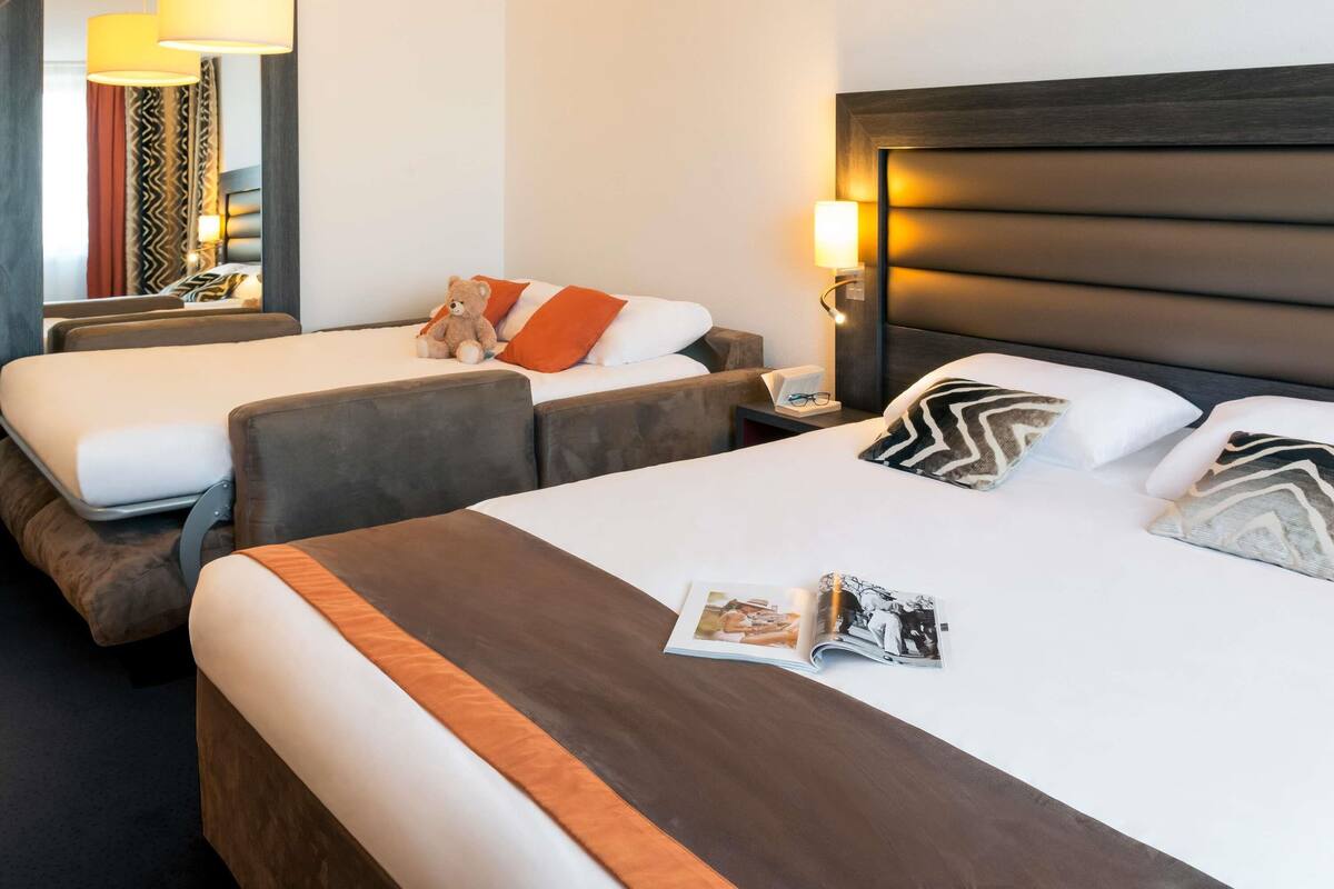 A hotel room with two beds, a large mirror, and a bedside table with a lamp.