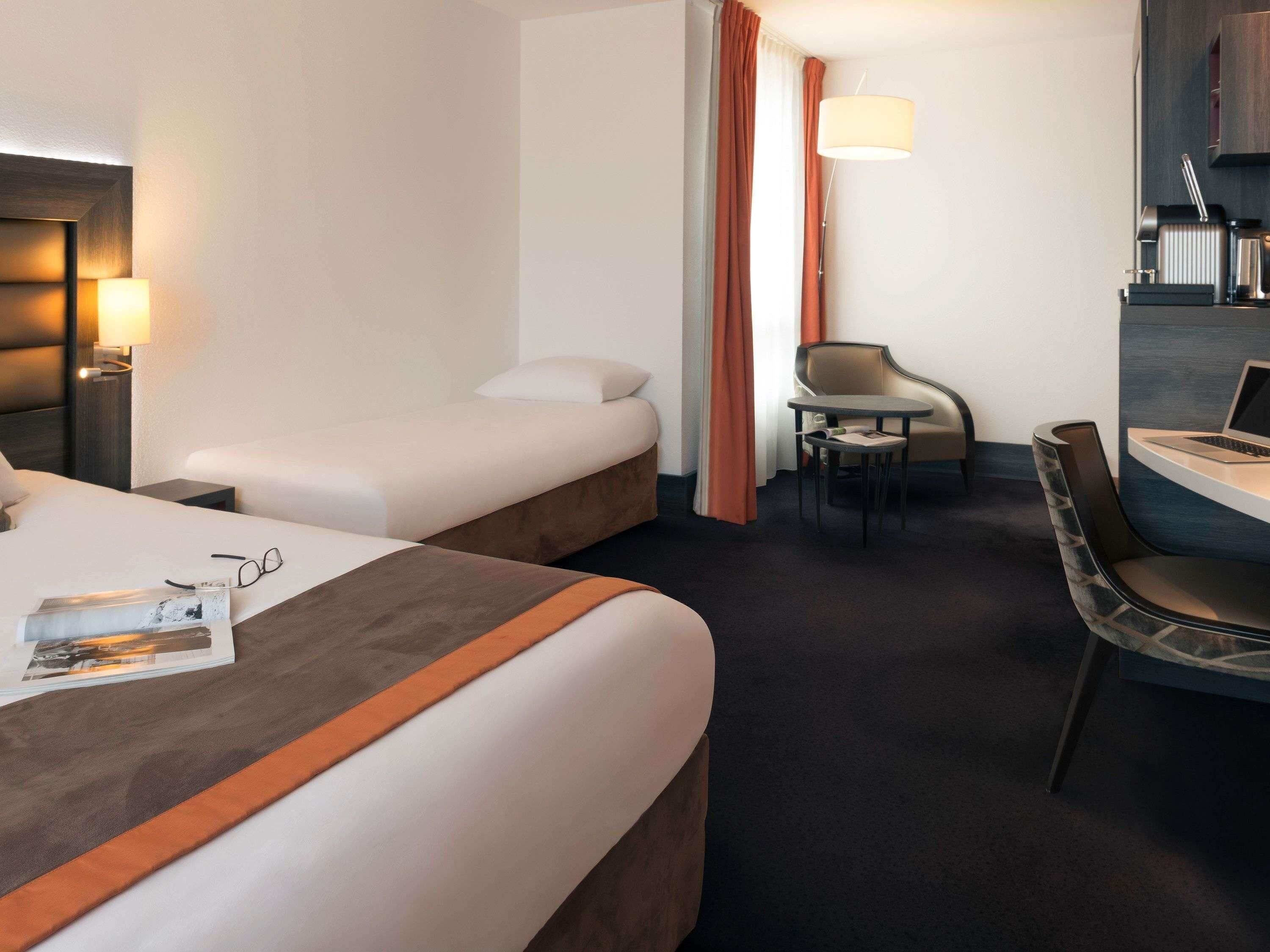 A hotel room with two beds, a desk with a chair, a lamp, and a small table.