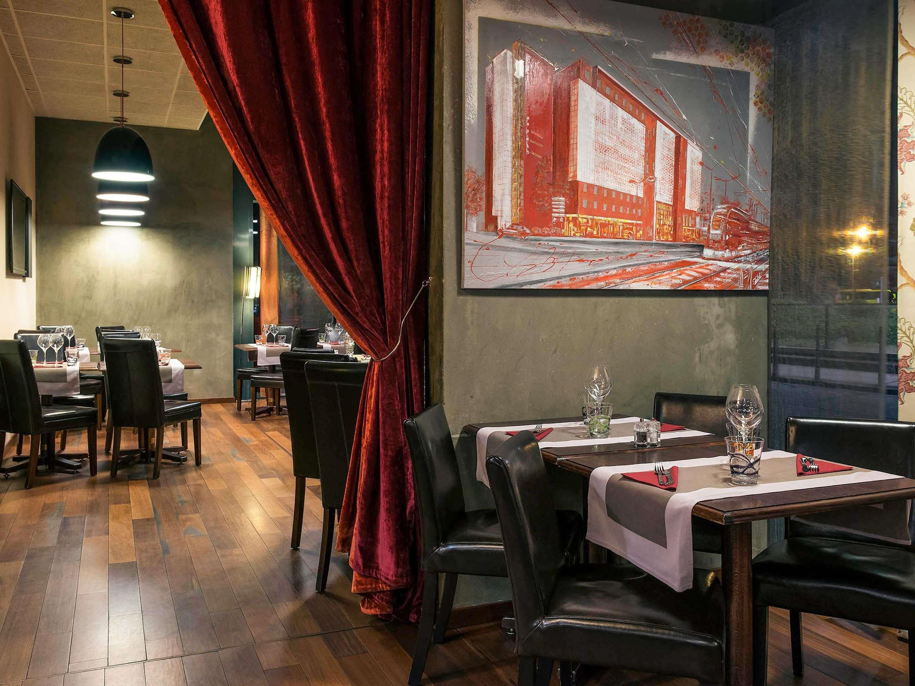 En restaurantindretning med borde dækket til spisning, en rød gardin og et maleri på væggen.
