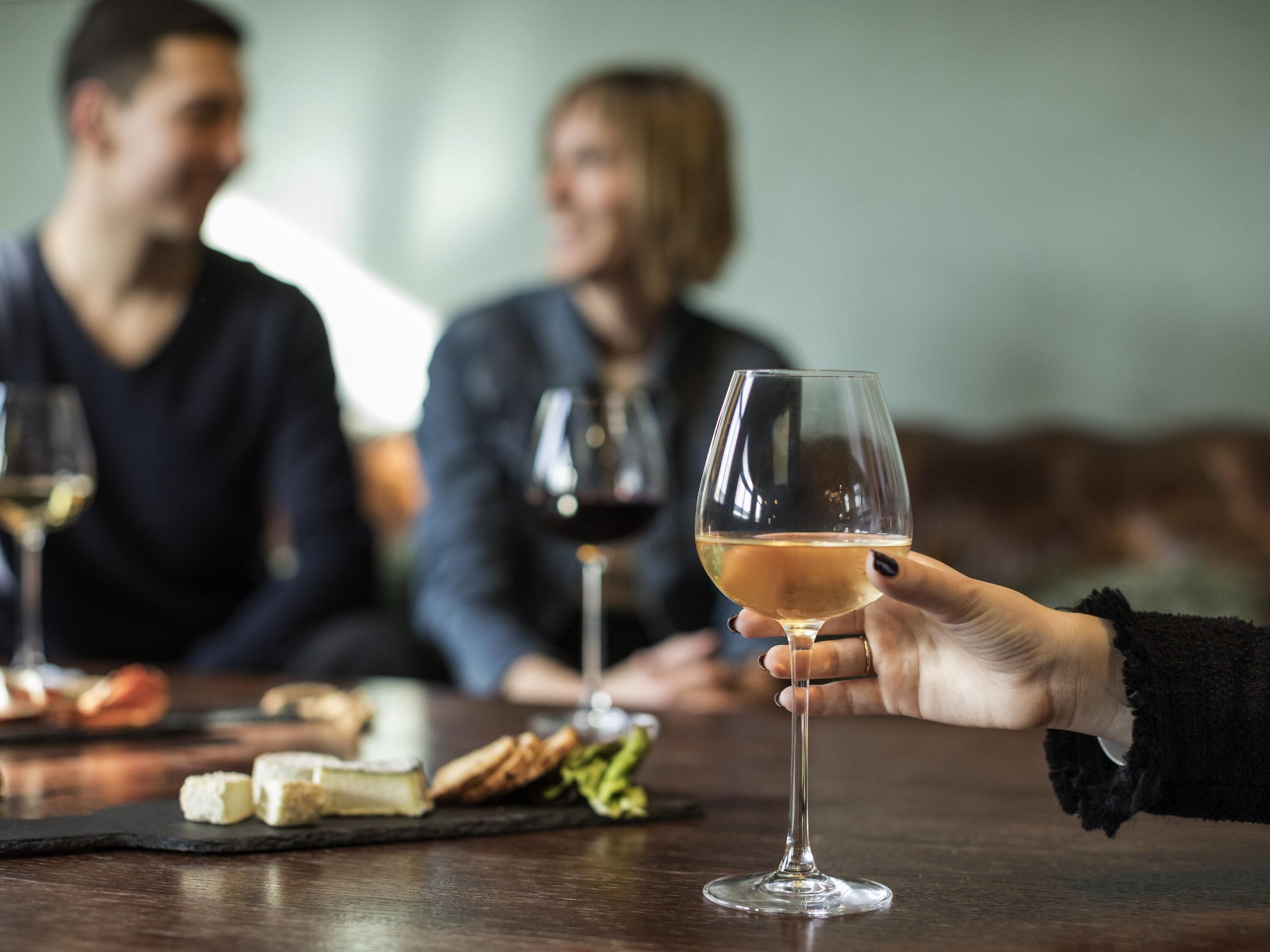 A person holding a wine glass at a dining table with cheese and crackers.