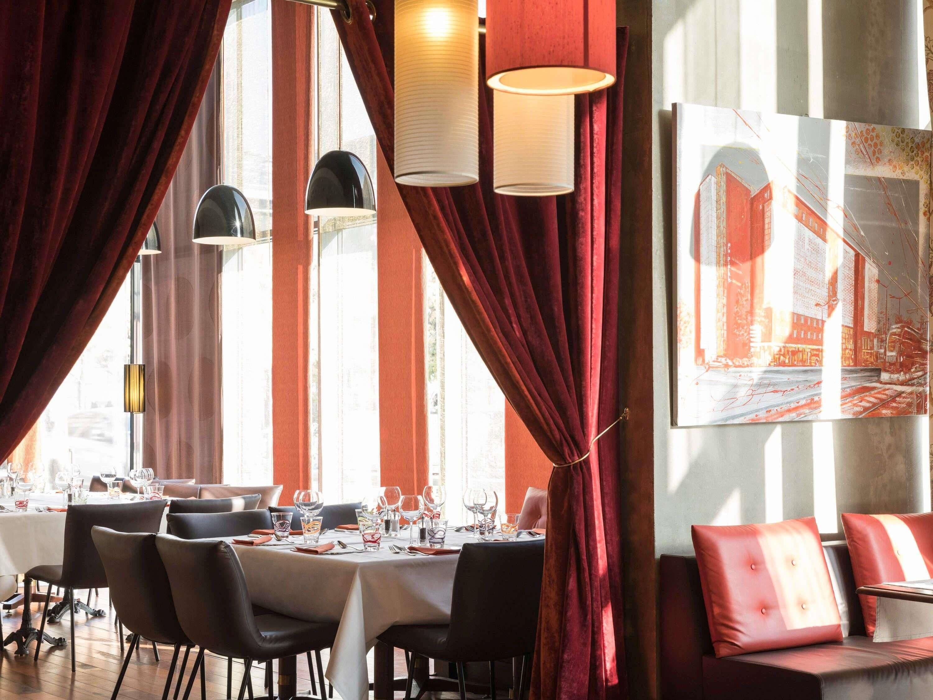 Ein Restaurantinneres mit einem Essbereich, roten Vorhängen und einem großen Gemälde an der Wand.