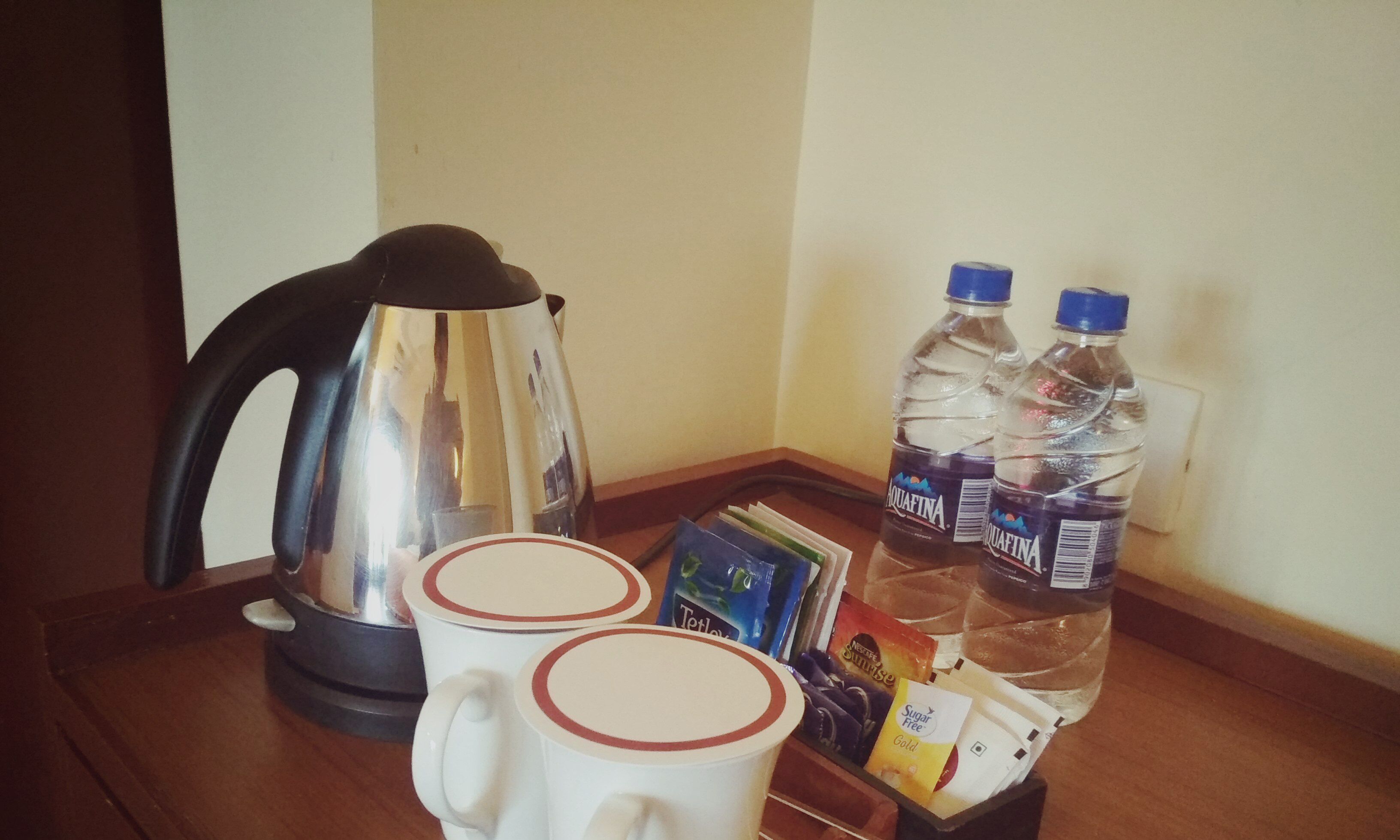Une machine à café, deux bouteilles d’eau, un plateau avec des capsules de café et deux tasses sur une table en bois.