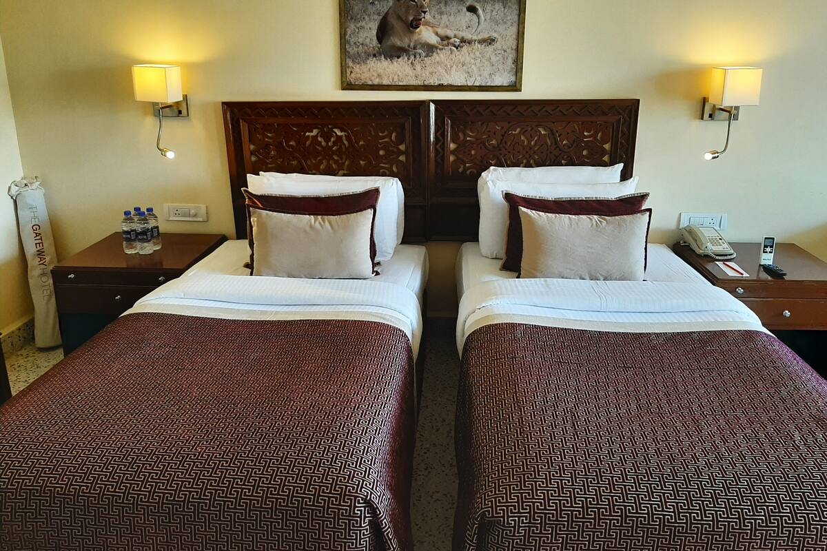 A hotel room with two beds, a painting of a lion, wall-mounted lamps, and a telephone on the nightstand.