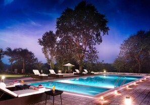 Ein Swimmingpool mit Liegestühlen und Sonnenschirmen, umgeben von Bäumen.