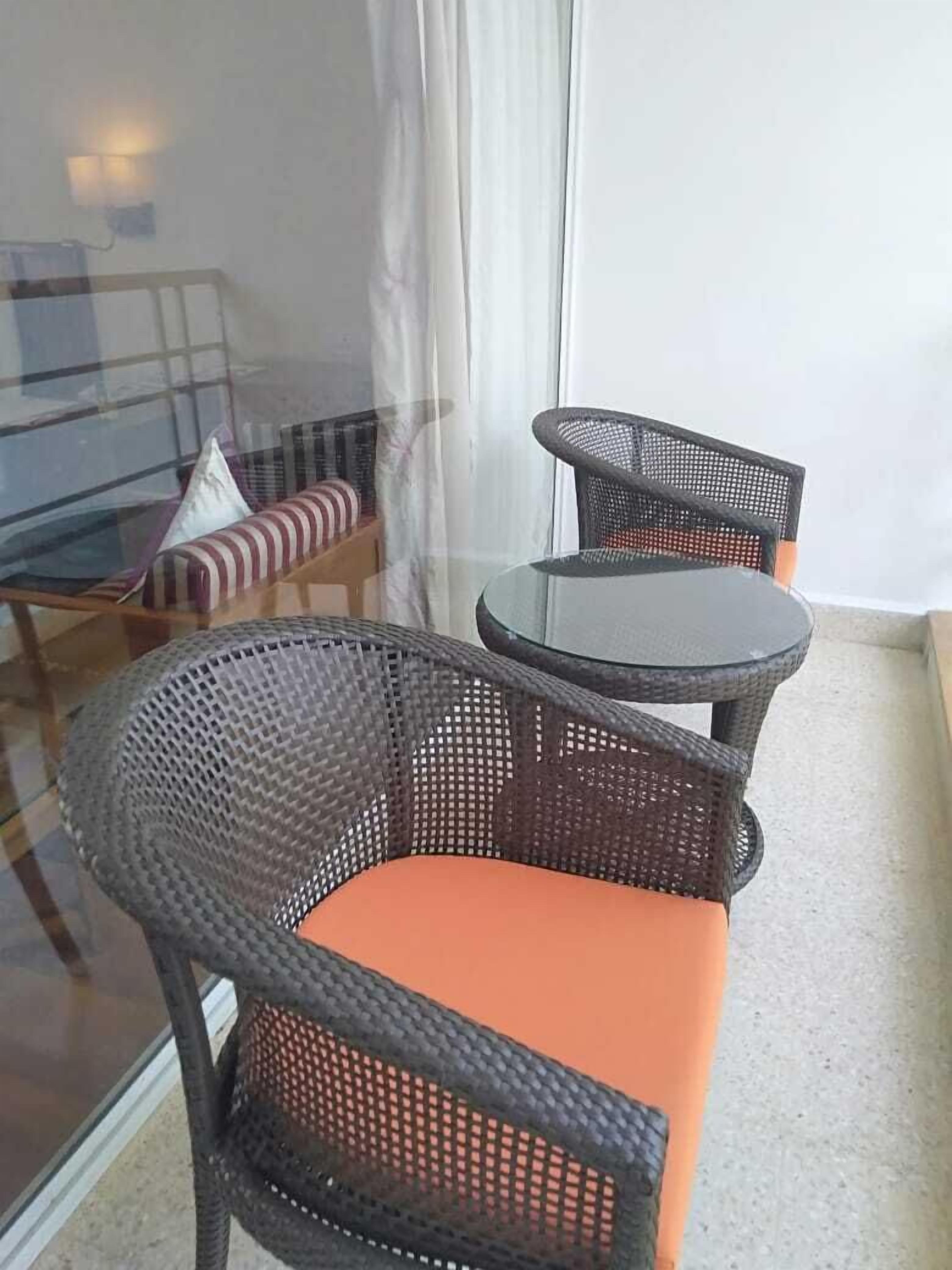 Un balcón con sillas de mimbre y una pequeña mesa.