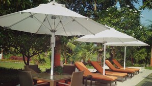 Outdoor lounge chairs and tables under white umbrellas, surrounded by lush greenery. - Gir Serai - IHCL SeleQtions (Mendarda)