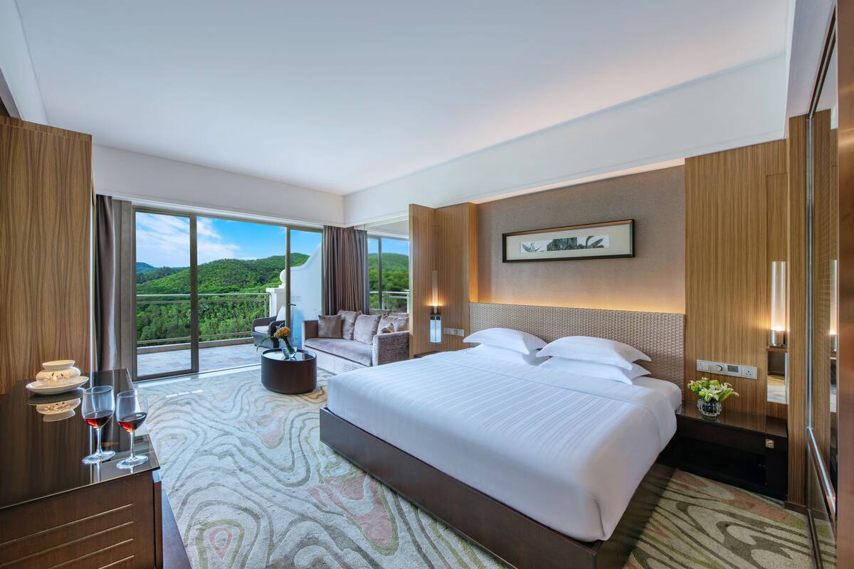 Una habitación de hotel moderna con una cama grande, un sofá, una mesa de comedor y vistas a las montañas.