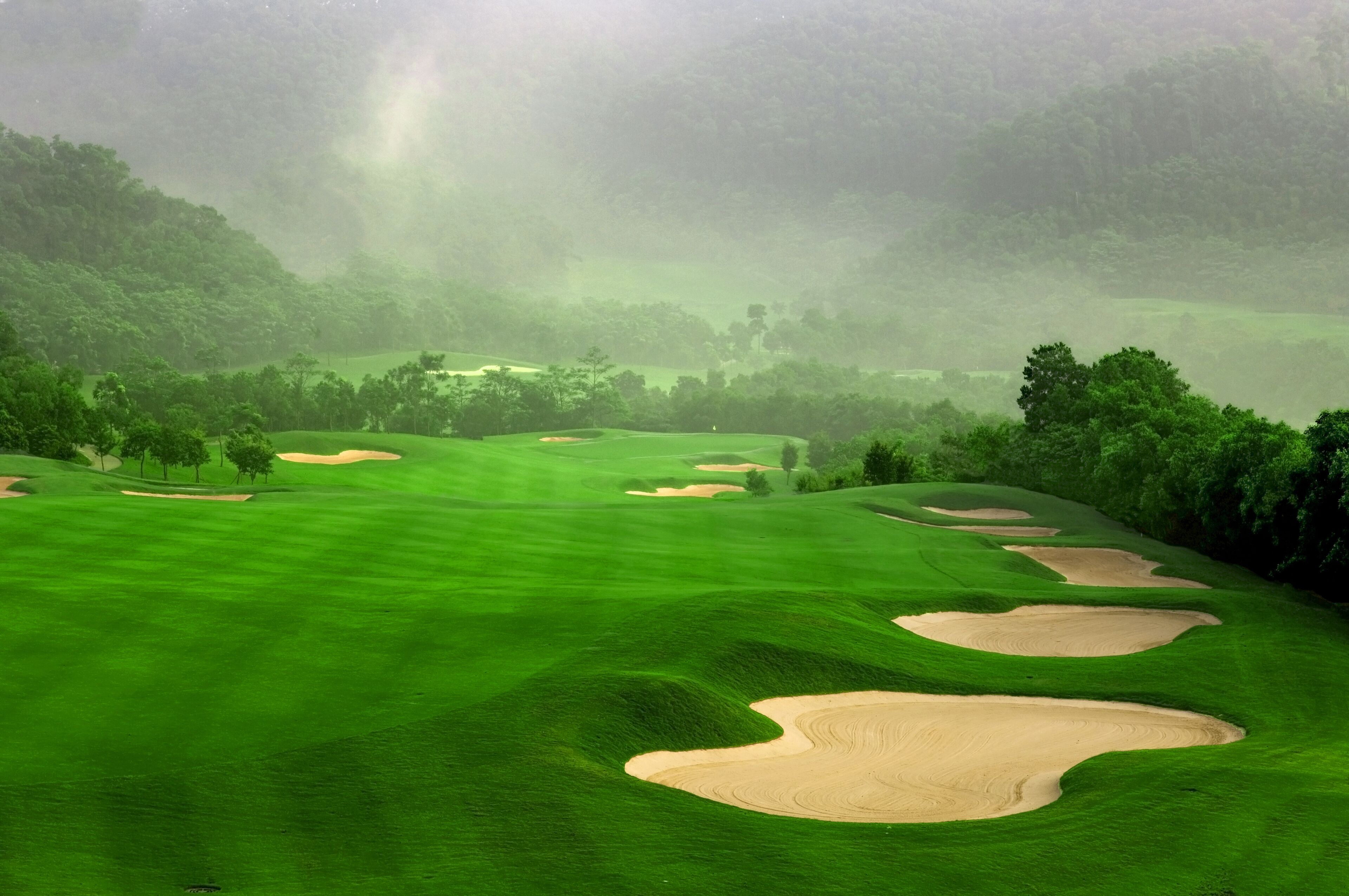 A golf course with well-maintained green fairways and sand bunkers.