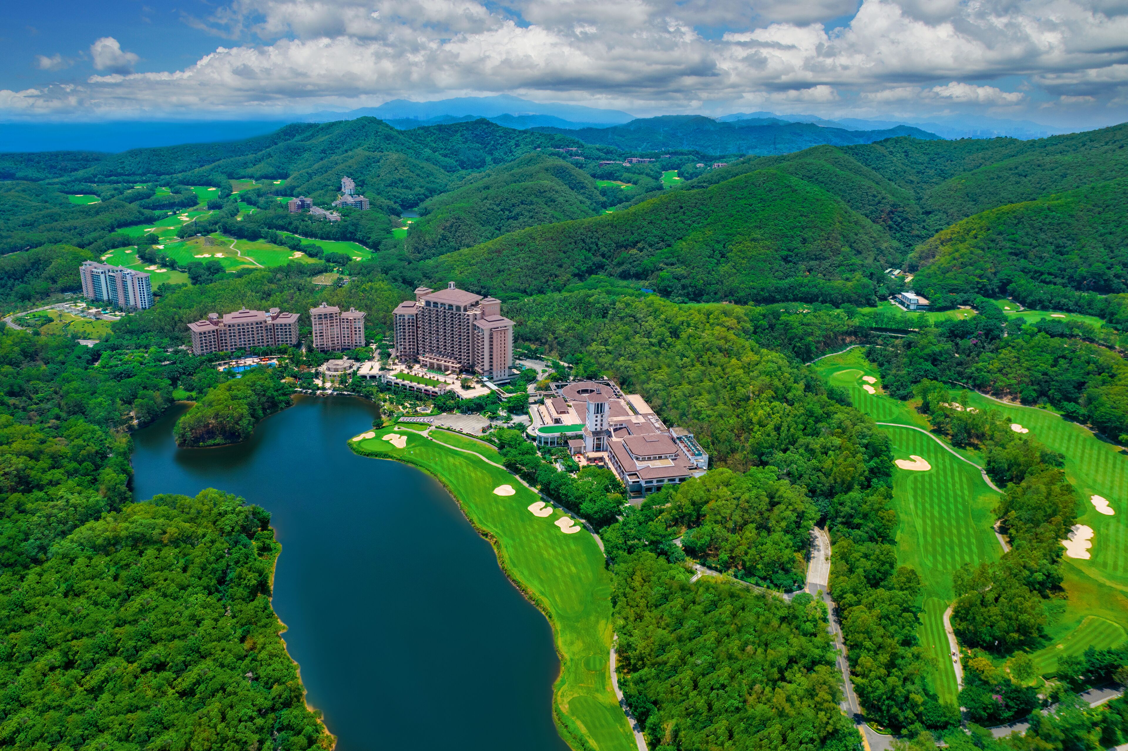 An aerial view of a golf course with multiple buildings, a lake, and surrounding hills.
