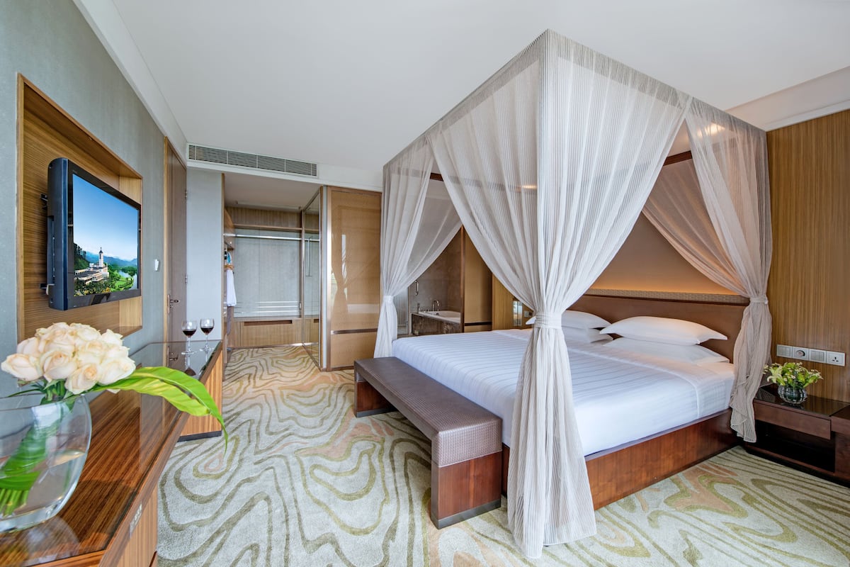 Una habitación de hotel moderna con una cama grande, un televisor montado en la pared, un escritorio de madera y un banco.