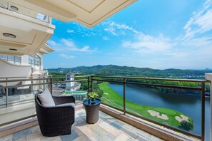 Un balcon agrémenté de meubles en osier, d’une plante en pot et offrant une vue sur un terrain de golf et un lac.