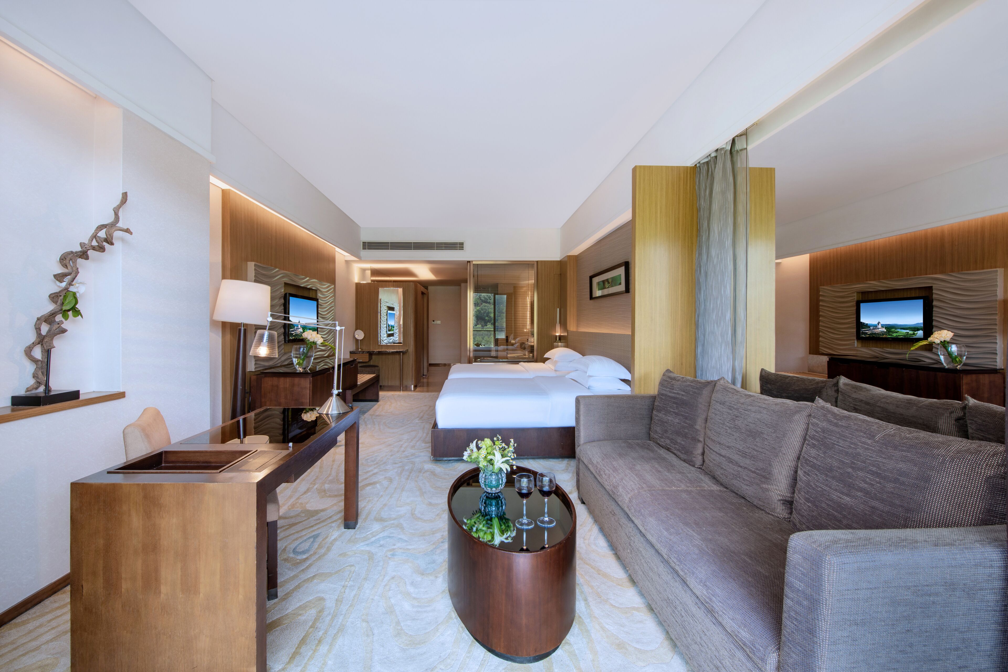 A modern hotel room with a large bed, a sofa, a desk, and a television.