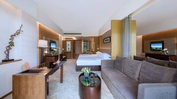 A modern hotel room with a large bed, a sofa, a desk, and a television.
