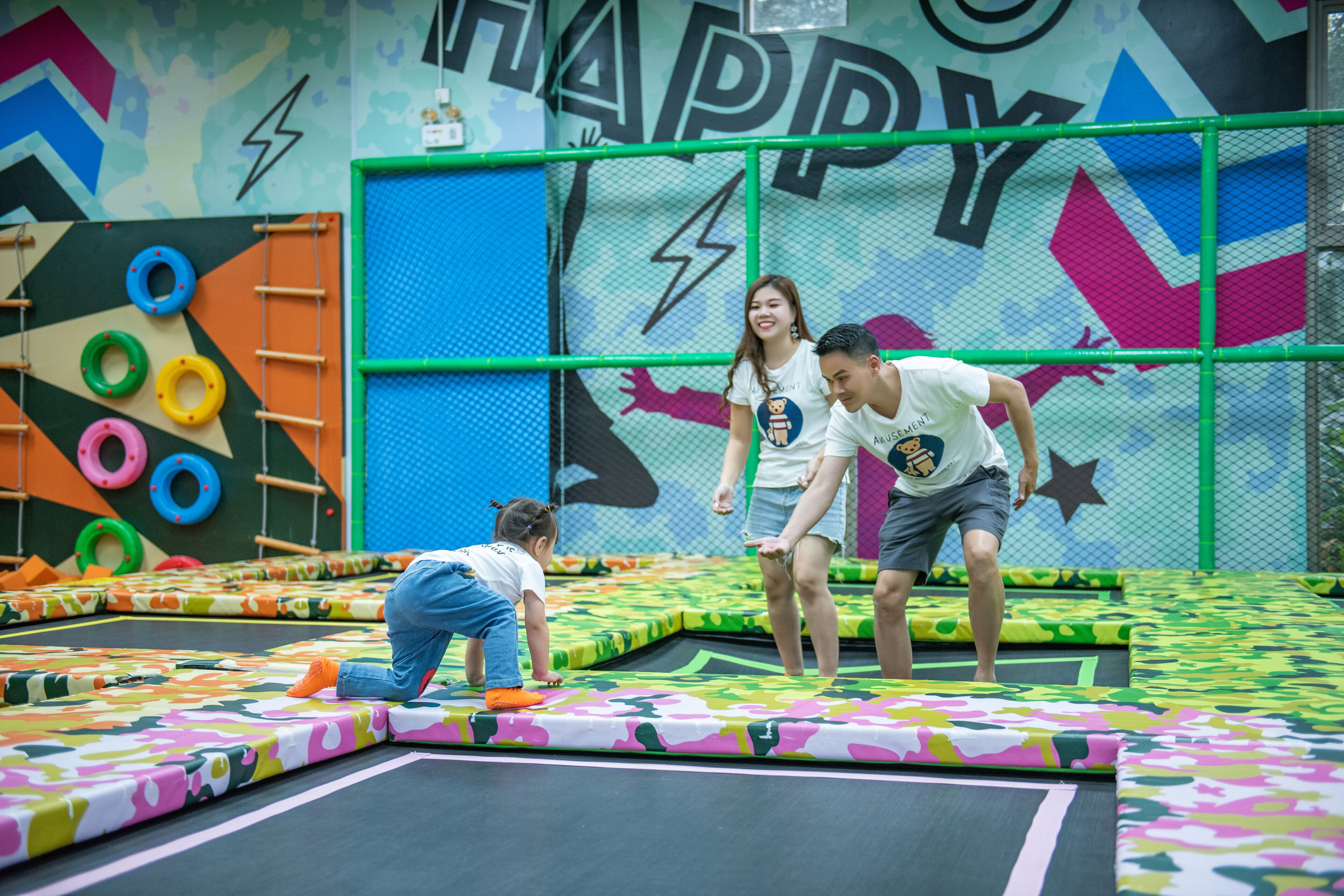 Zona de trampolines amb estores de colors i una paret amb el lema 'HAPPY'.