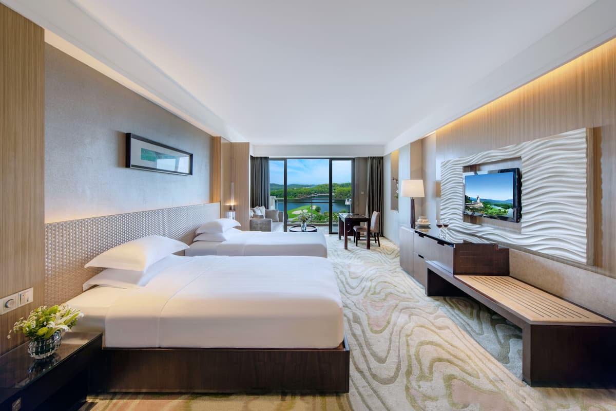 Habitación de hotel con dos camas, televisión, escritorio y vista al exterior.