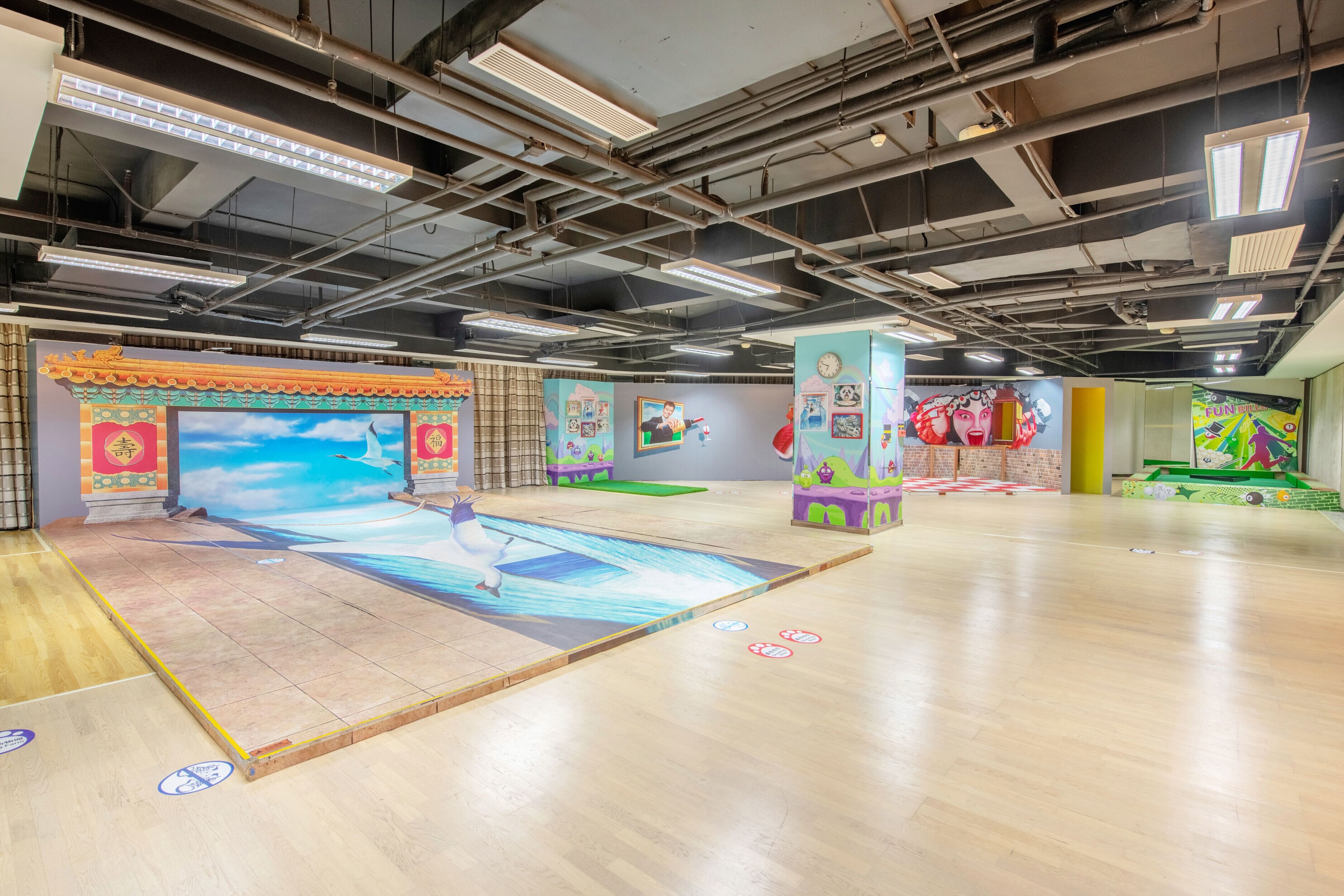 A spacious indoor area with a large mural, wooden flooring, and various colorful play structures.