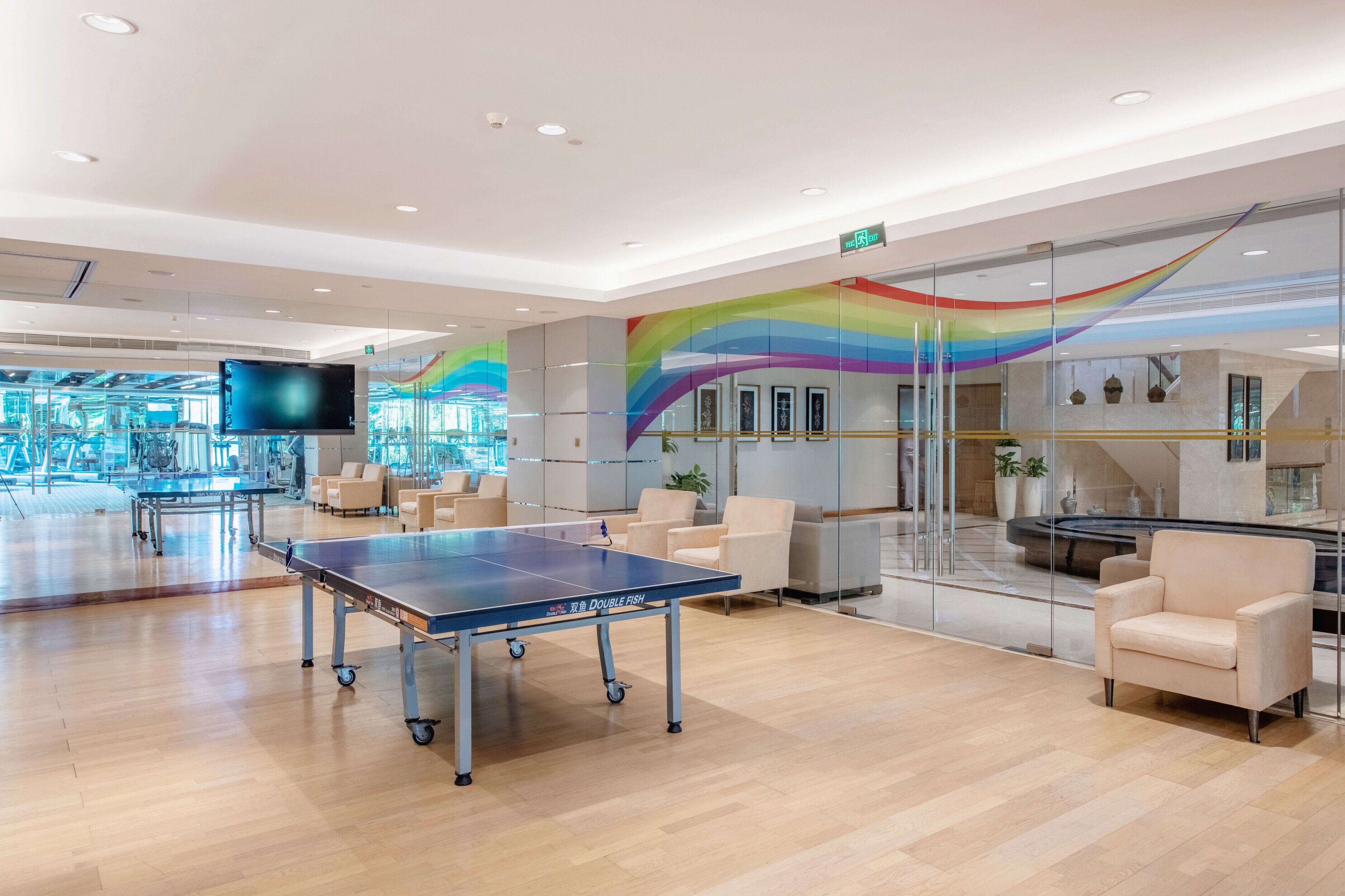 A modern indoor space with a ping pong table, comfortable seating, and a glass wall with a rainbow design.