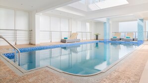 A large indoor swimming pool with clear blue water, surrounded by lounge chairs and a tiled floor. - Al Hail Waves Hotel Managed By Centara (Seeb)
