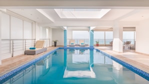 A modern indoor swimming pool with clear blue water, sunlit ceiling, and lounge chairs along the poolside. - Al Hail Waves Hotel Managed By Centara (Seeb)