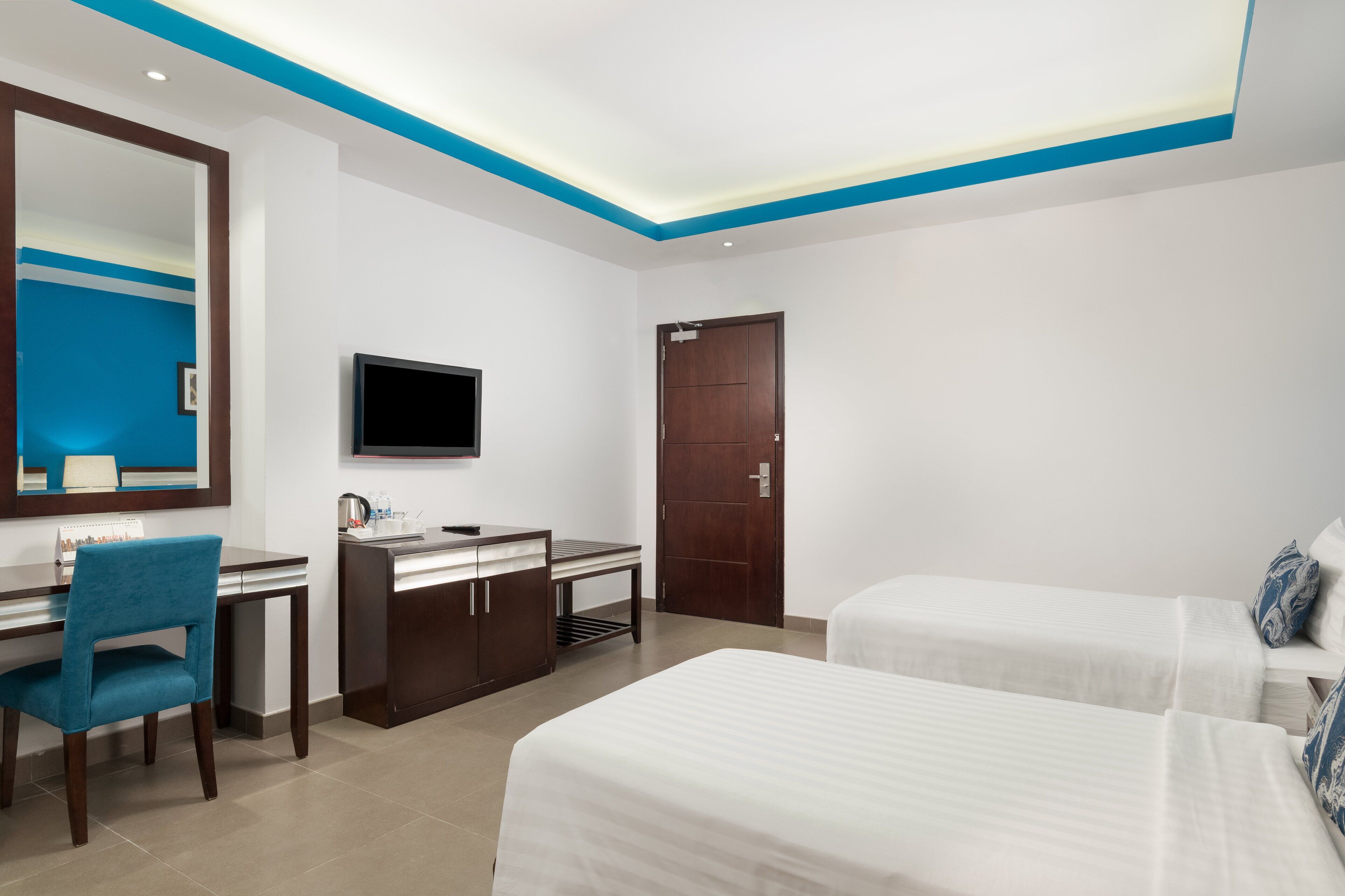 A hotel room with a desk, chair, TV, and two beds.