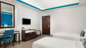 A hotel room with a desk, chair, TV, and two beds.