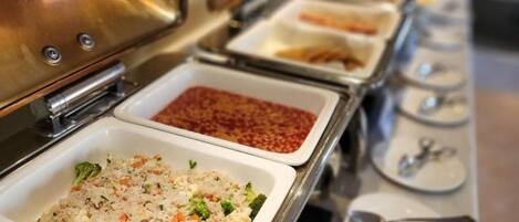 A buffet line with various dishes, including rice with vegetables and a red sauce.