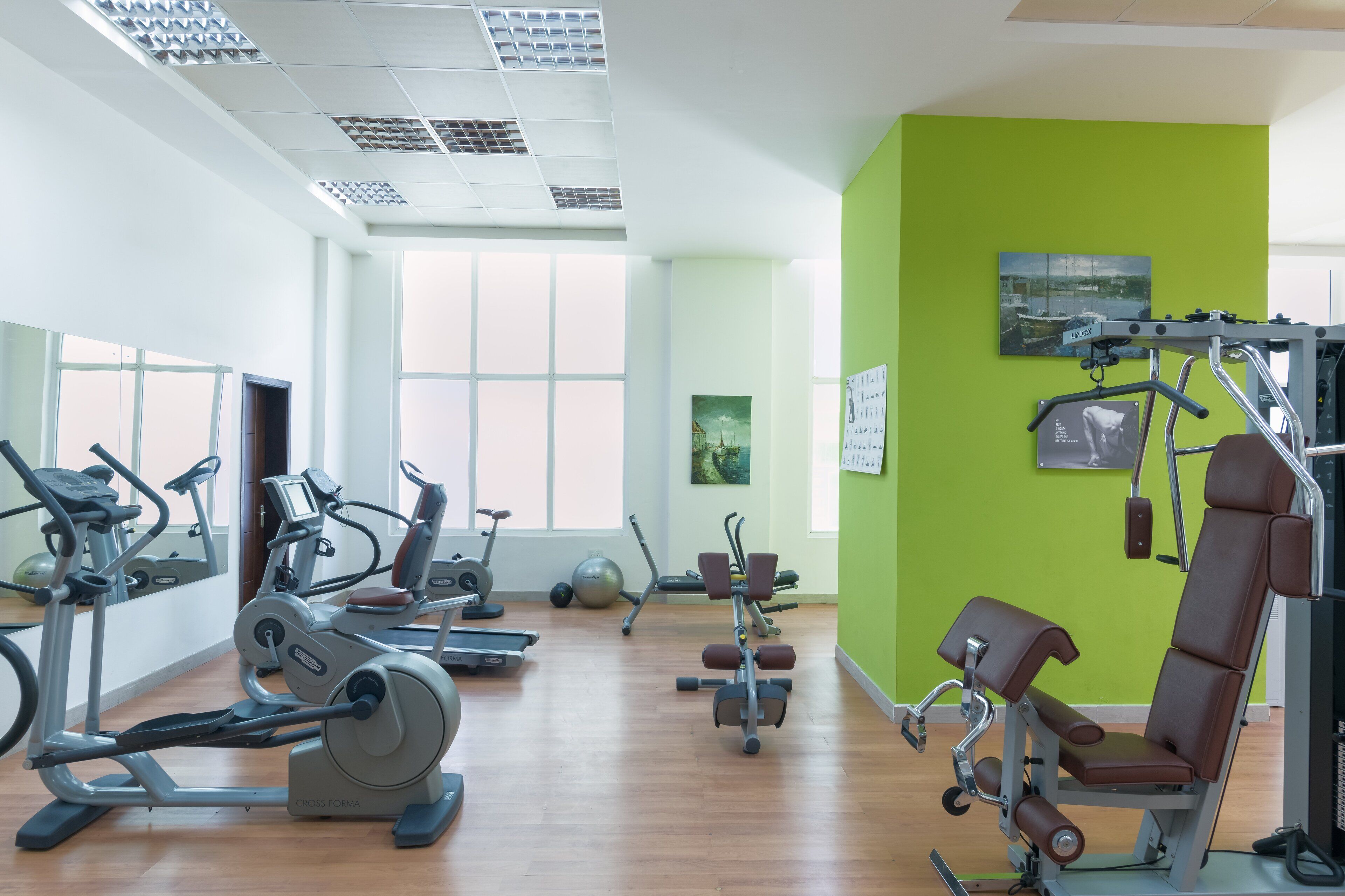 A gym with cardio machines, weight equipment, and a green wall.