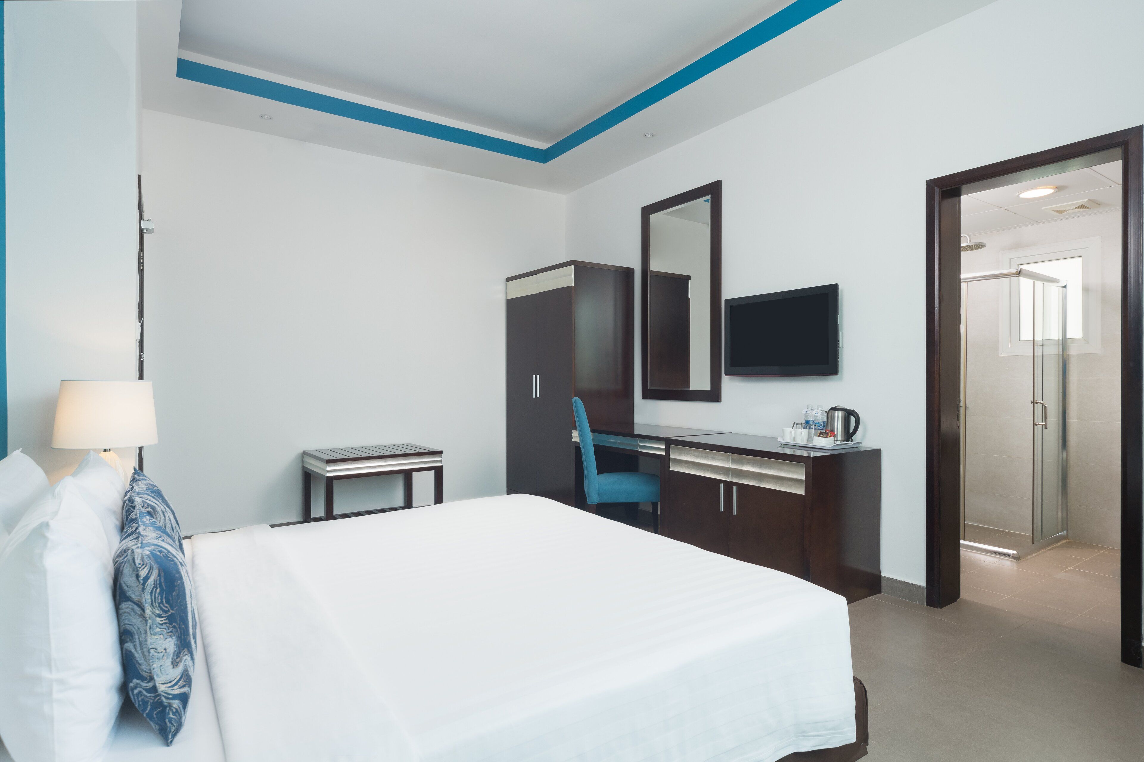 A hotel room with a bed, a desk, a chair, a mirror, a TV, and a bathroom visible through an open door.