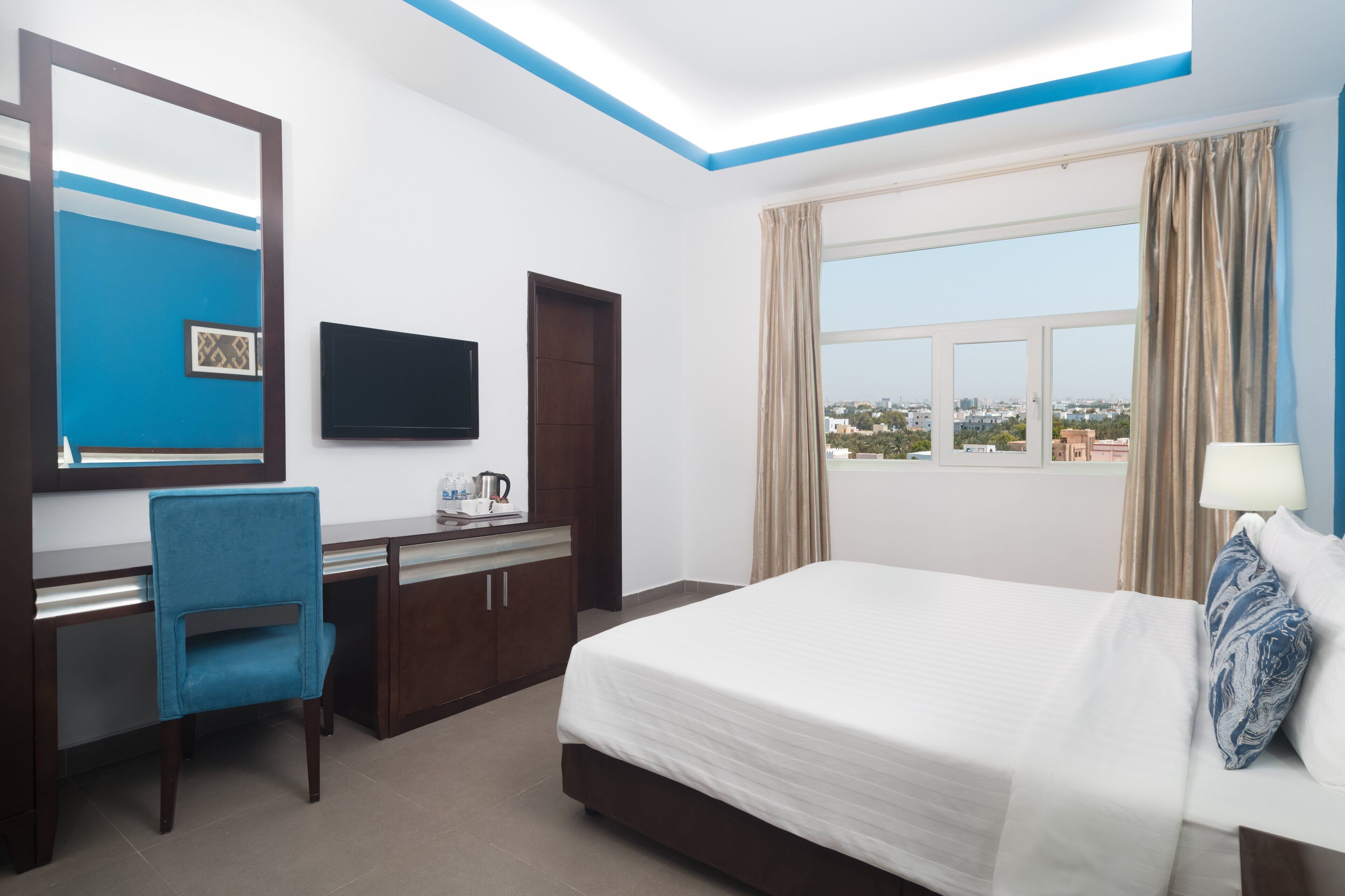 Ein Hotelzimmer mit Bett, Schreibtisch, Stuhl, Fernseher und einem Fenster mit Blick auf die Stadt.
