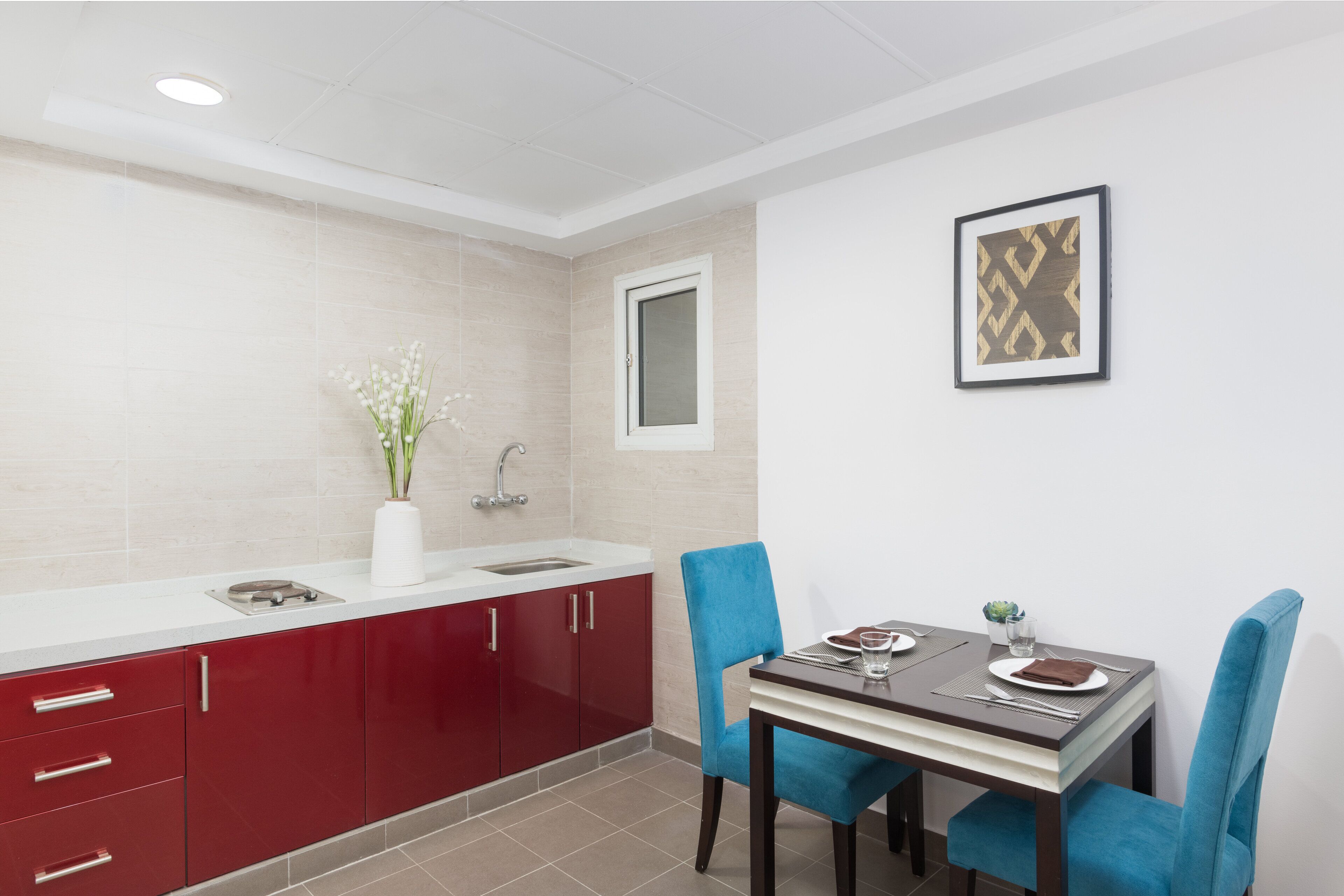 A modern kitchen with red cabinets, a white countertop, and a dining area with a table and blue chairs.