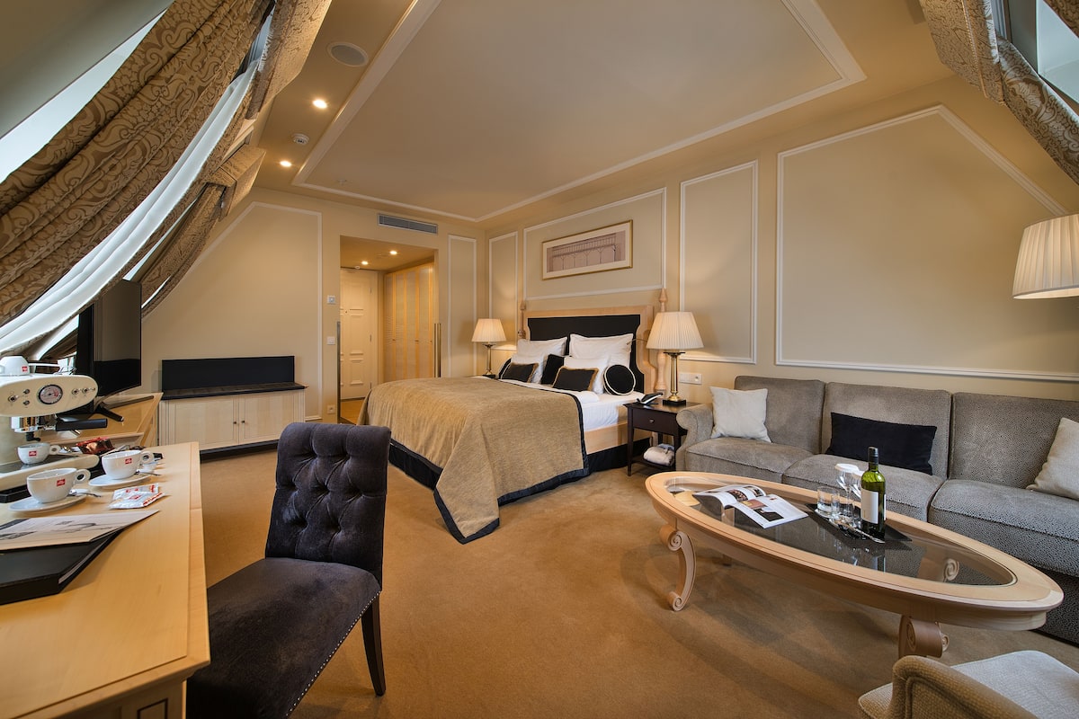 A hotel room with a bed, a sofa, a coffee table, a desk with a computer, and a television.
