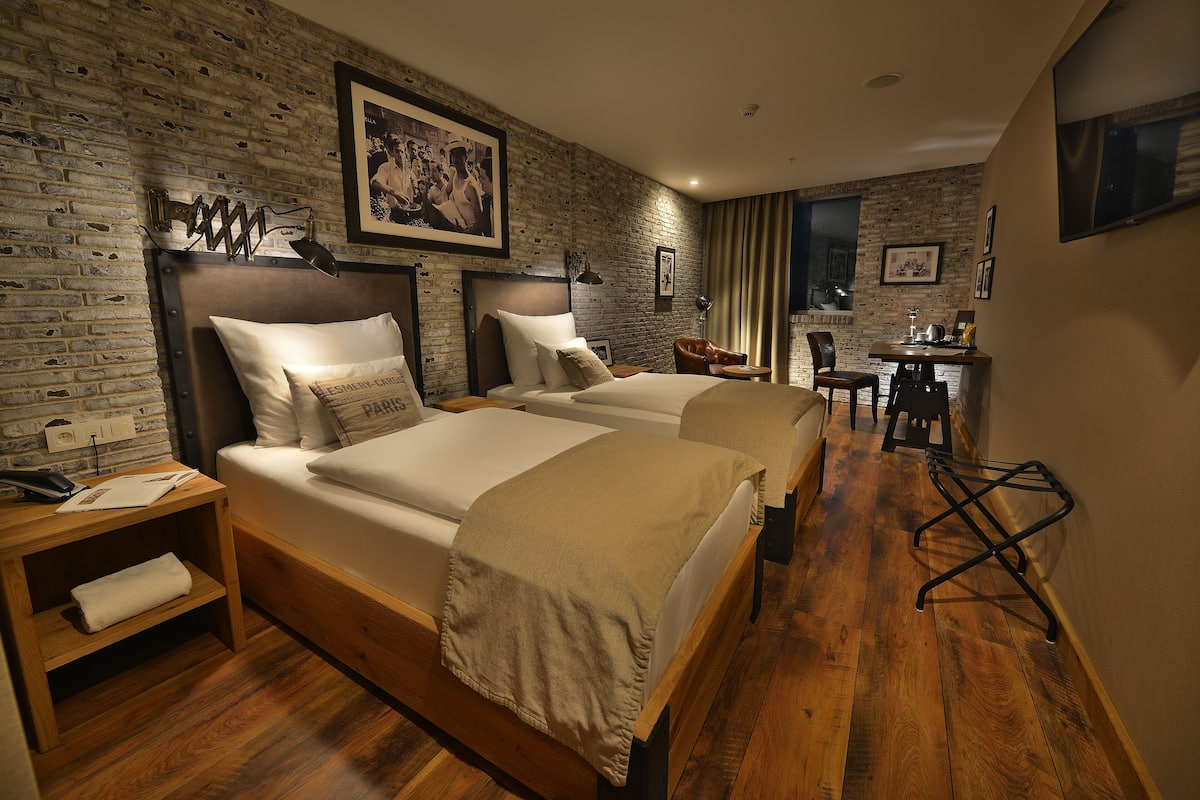 A hotel room with a brick wall, two beds, a desk, and a chair.