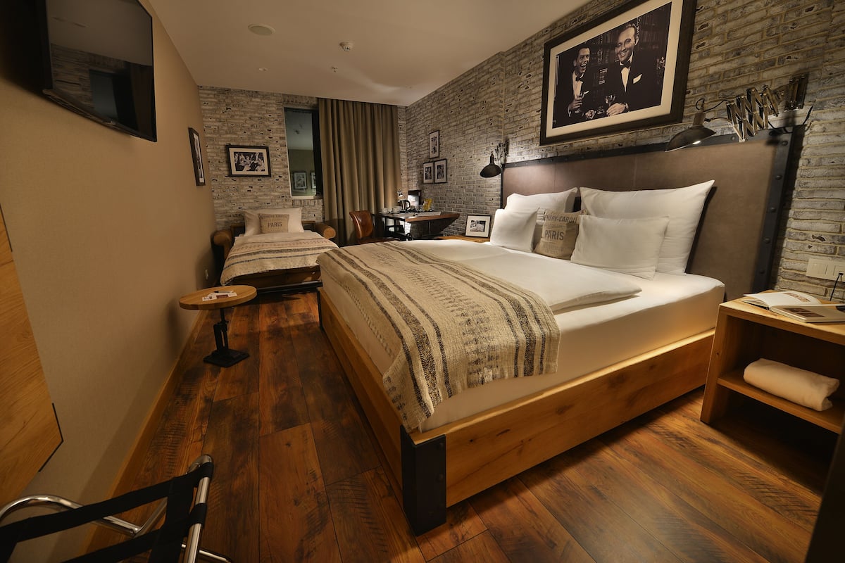 A modern hotel room with a wooden bed, a desk, a chair, and a small table.