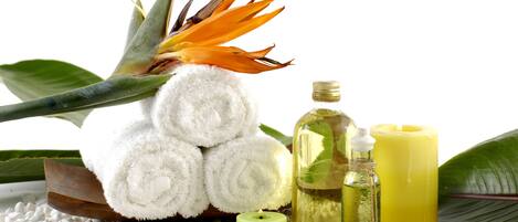 Un décor de spa avec une serviette blanche roulée, une bougie verte, une bougie jaune et une bouteille d’huile.