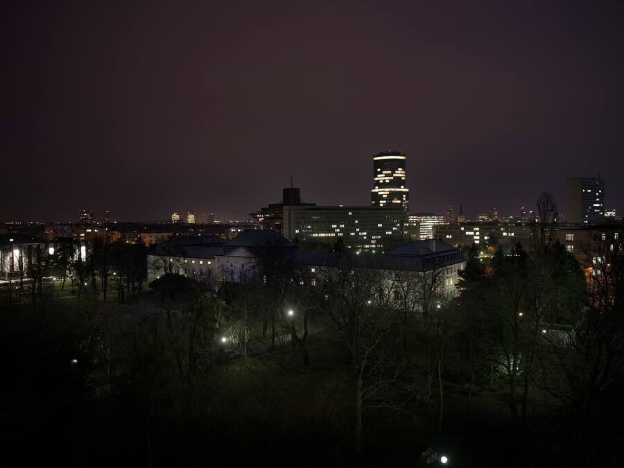 Paisagem urbana noturna com edifícios iluminados e uma área de parque.
