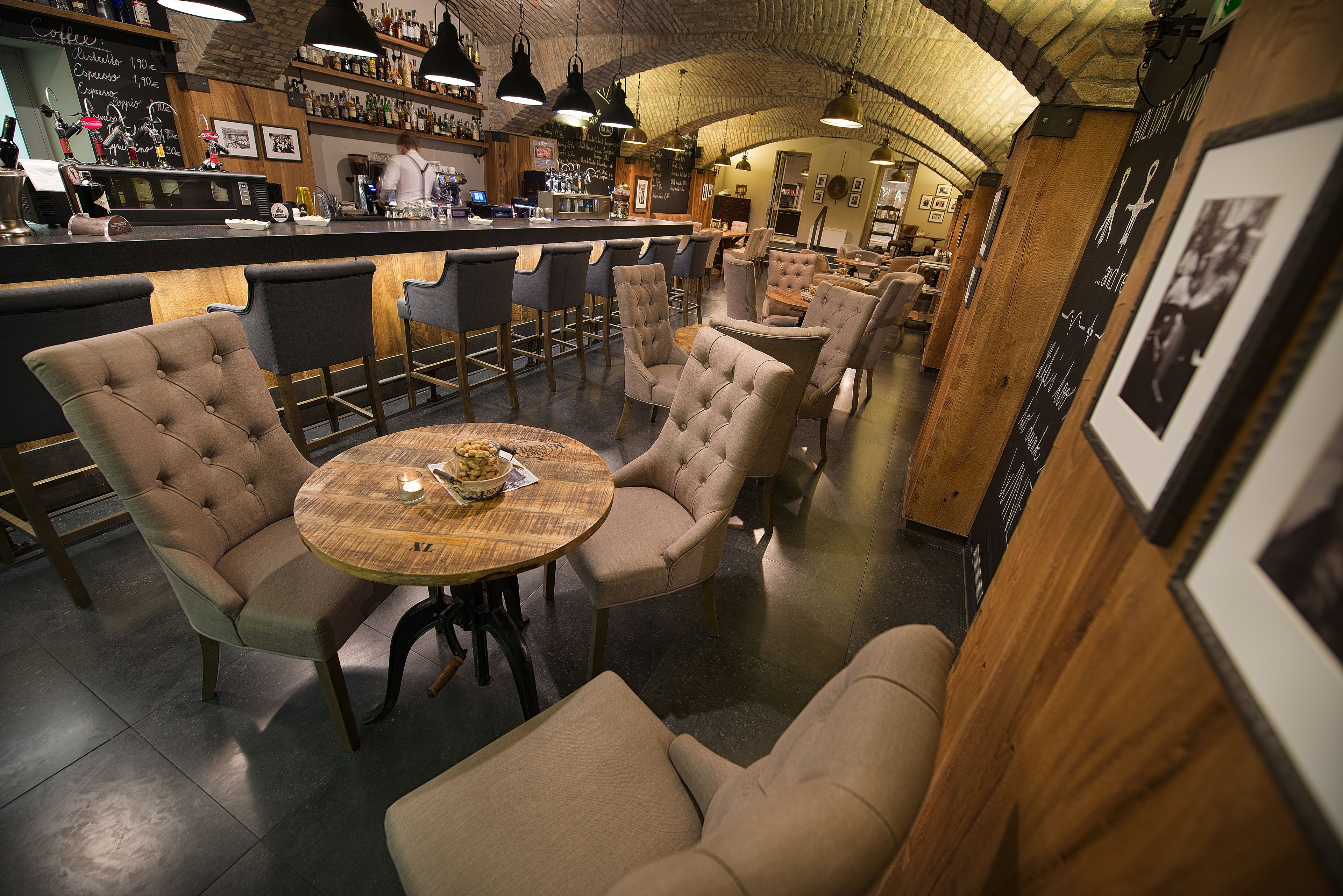 Zona de bar con taburetes altos, una mesa redonda con un cuenco de aceitunas y una barra con una carta.