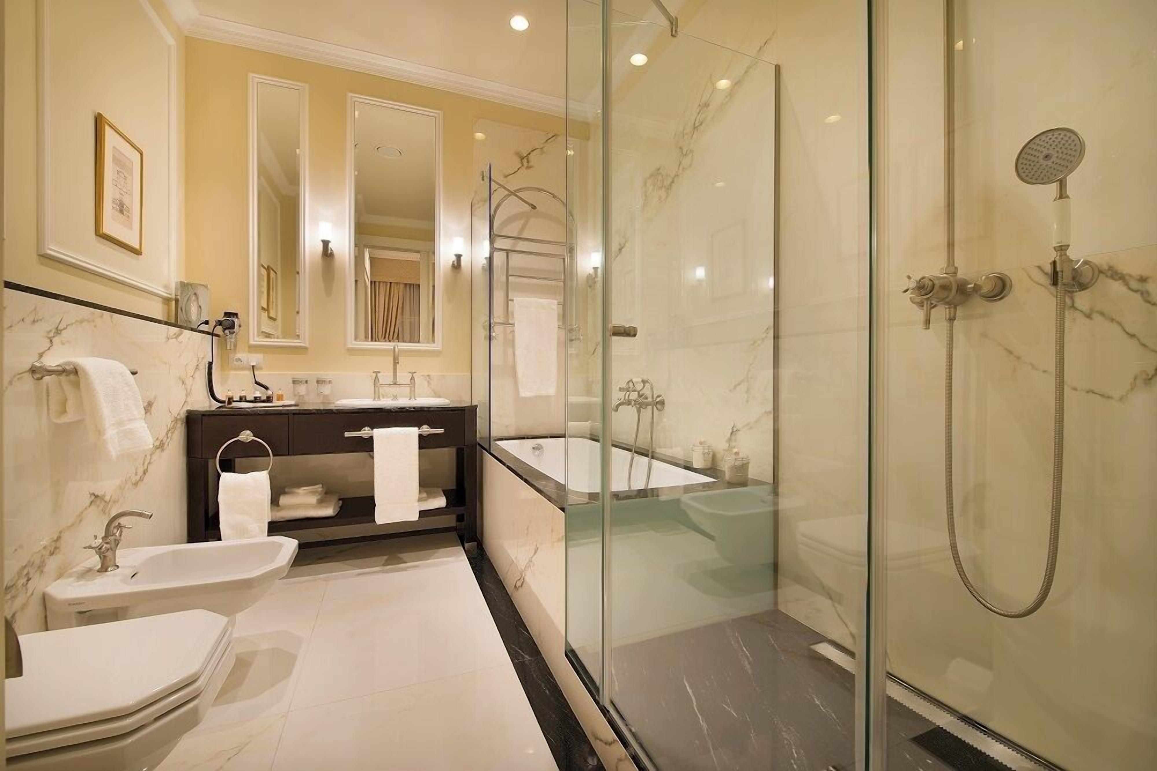 A modern bathroom with a glass-enclosed shower, a bathtub, and two sinks.