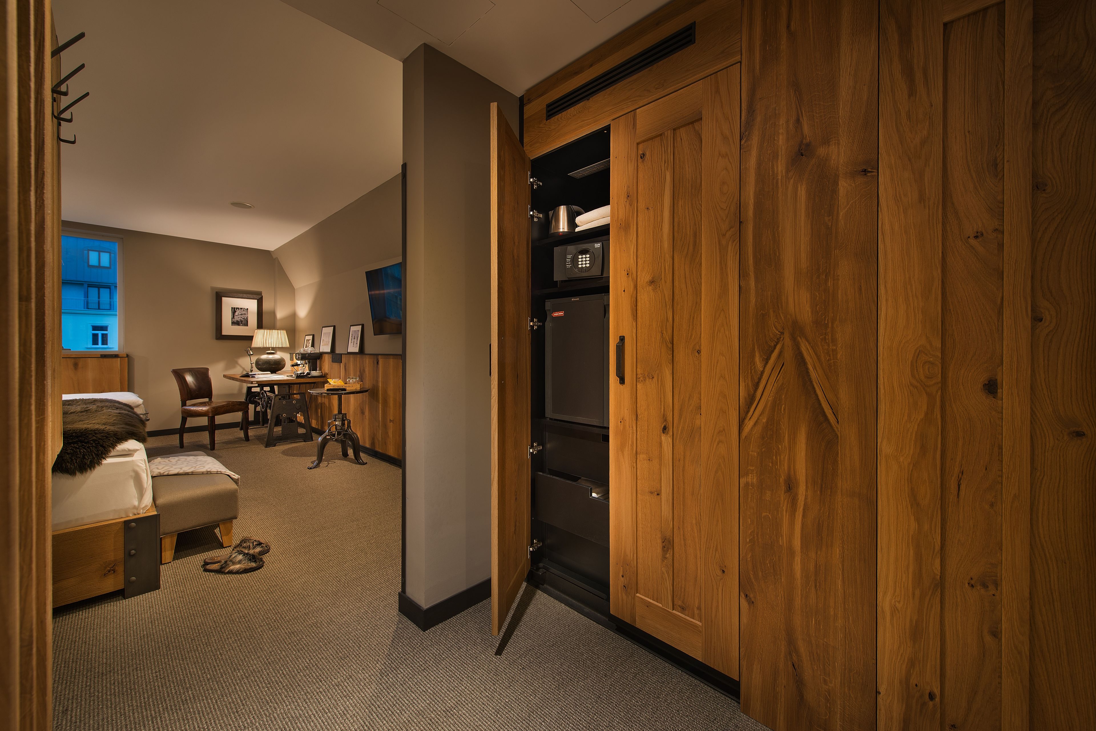 A hotel room with a wooden wardrobe, a bed, a desk, and a chair.