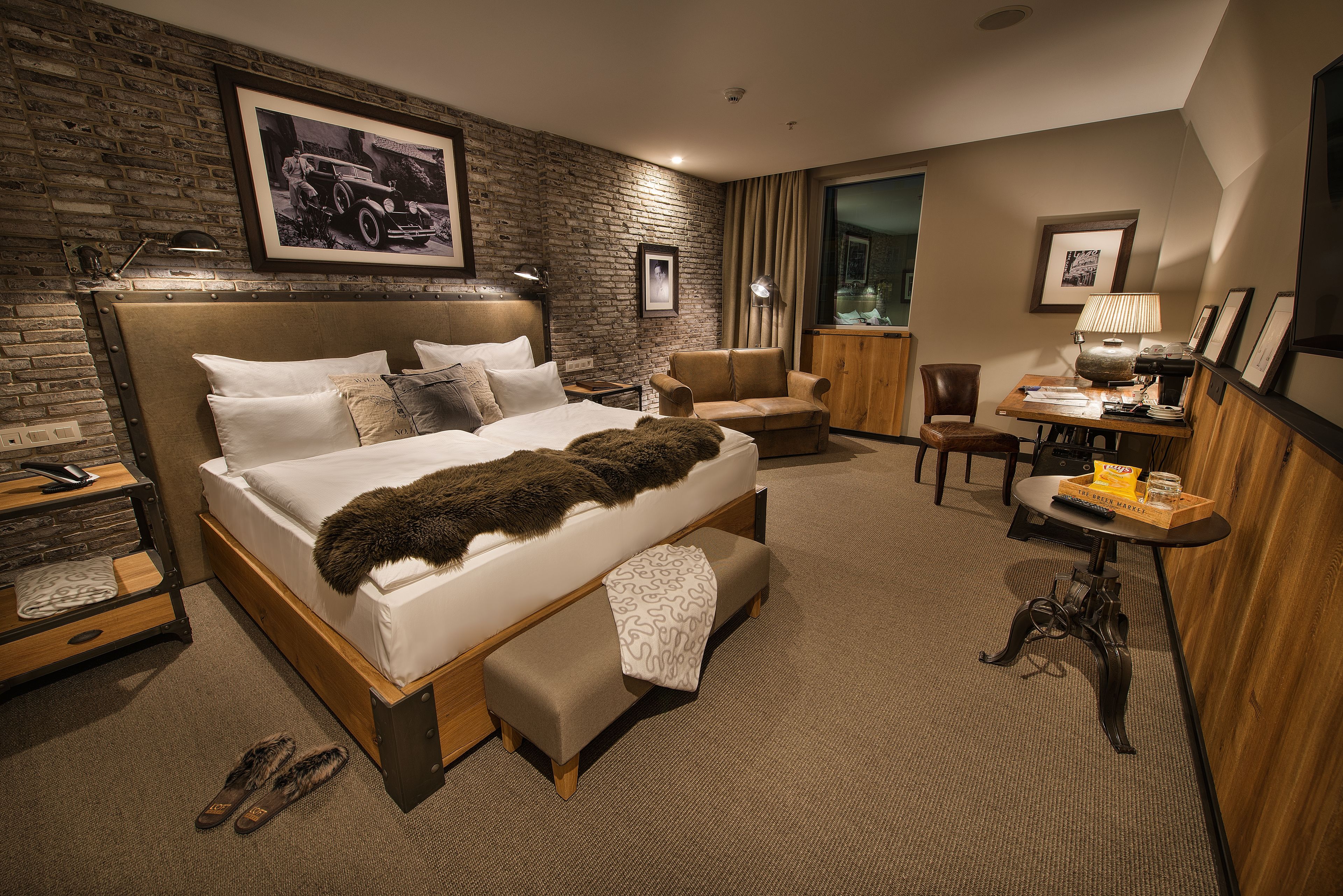 A hotel room with a large bed, a wooden bench, a desk, and a chair.