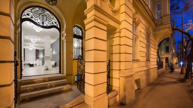 Una entrada imponente con escalones que conducen a un interior bien iluminado, con un amplio arco y detallada rejería.
