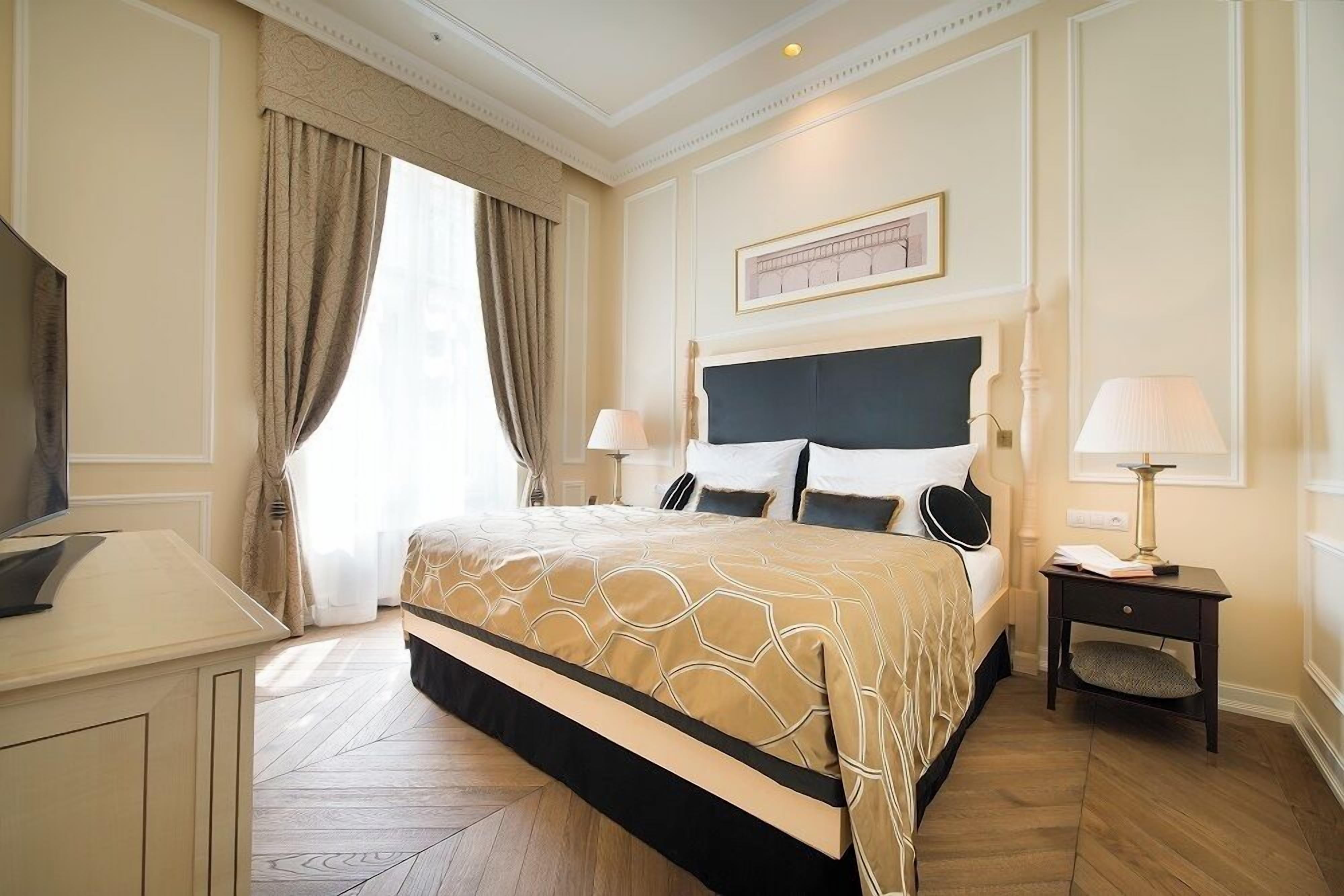 A hotel room with a large bed, a desk, a chair, a nightstand with a lamp, and a framed picture on the wall.
